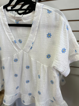 Neckline detail of the white top with blue and yellow daisies embroidery 