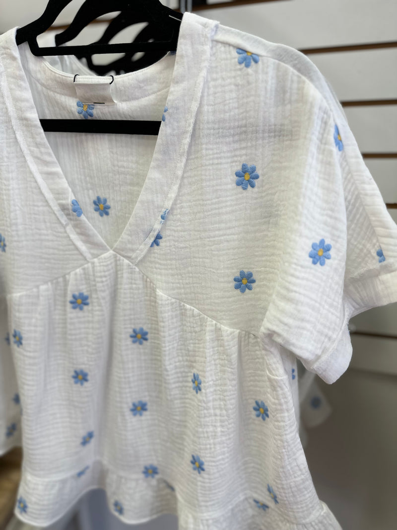 Neckline detail of the white top with blue and yellow daisies embroidery 